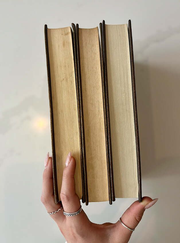 bloc de livre (trois) qu'une main tiens, sur un comptoir blanc.