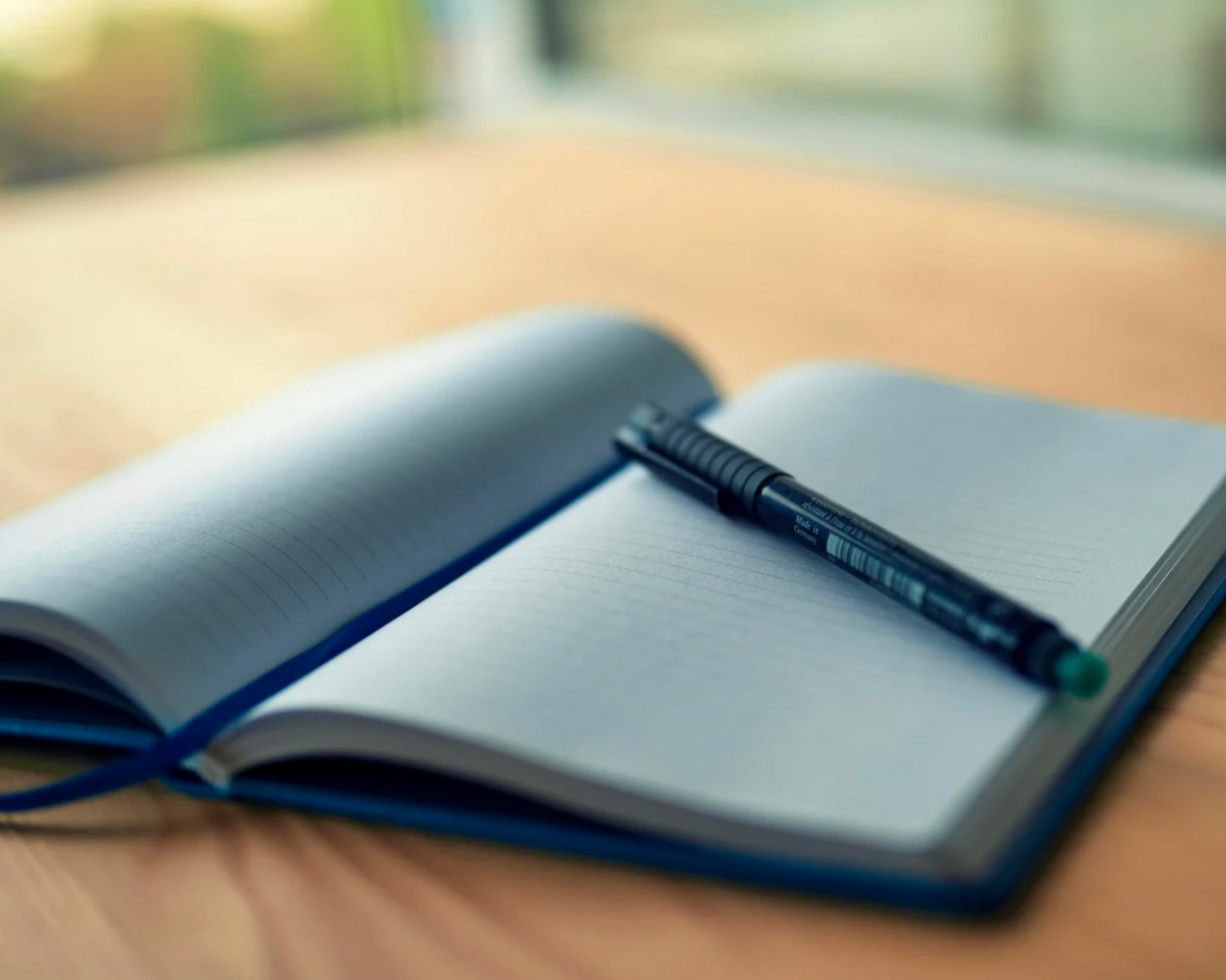 Table en bois, avec un calepin ouvert sur des pages blanches accompagné d'un crayon.