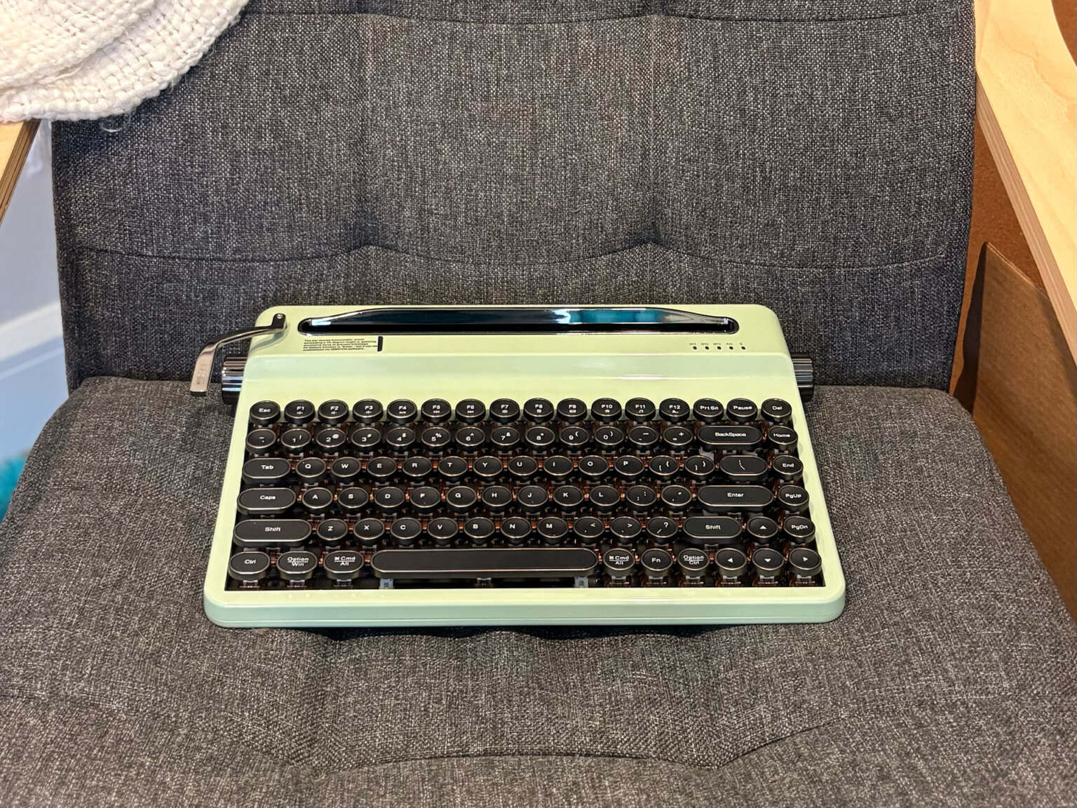 Une machine à écrire vert menthe sur divan gris foncé.